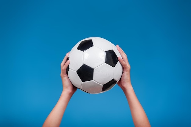 Pallone da calcio tenuto dalle mani di un bambino isolato su sfondo blu Concetto di sport