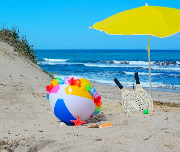 Pallone da spiaggia con collana racchette e ombrellone in riva al mare