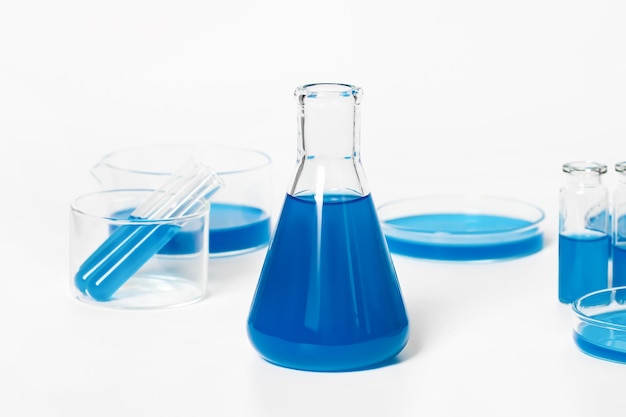 Pallone per il laboratorio con un liquido blu blu Sullo sfondo di vetreria da laboratorio Petri provette per boccette Su uno sfondo bianco chiaro