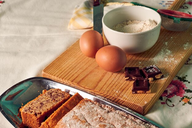 Pan di Spagna fatto in casa su una tovaglia bianca con alcuni ingredienti uova cioccolato e farina