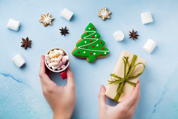 Pan di zenzero sotto forma di alberi di Natale su un blu, una tazza di cioccolata calda e caramelle nelle mani dei bambini.