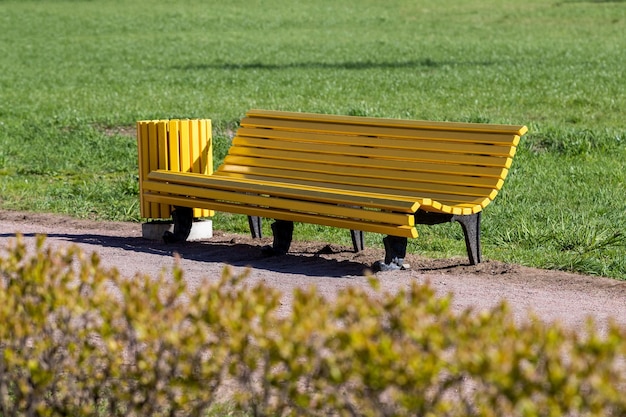 Panca gialla con un'urna nel parco sullo sfondo di erba verde e cespugli