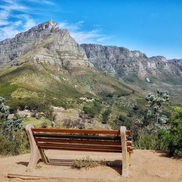 Panca in legno in una rilassante catena montuosa in un giardino botanico Parco nazionale di Table Mountain a Città del Capo in Sud Africa con cielo blu e posti a sedere locali per godersi la vista calma e zen di madre natura