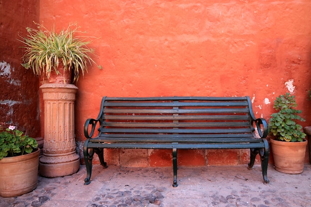 Panca in legno nero di fronte al muro grezzo di colore arancione con molte fioriere in terracotta, Perù