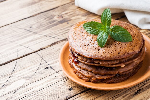 Pancake al cioccolato con marmellata di bacche e menta per la colazione sul tavolo di legno