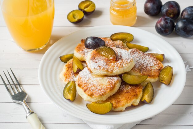 Pancake al formaggio in zucchero a velo con prugne fresche su un piatto