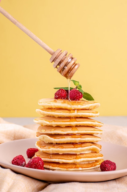 Pancake americani classici fatti in casa con lamponi freschi, more, miele e foglie di menta, su una superficie leggera