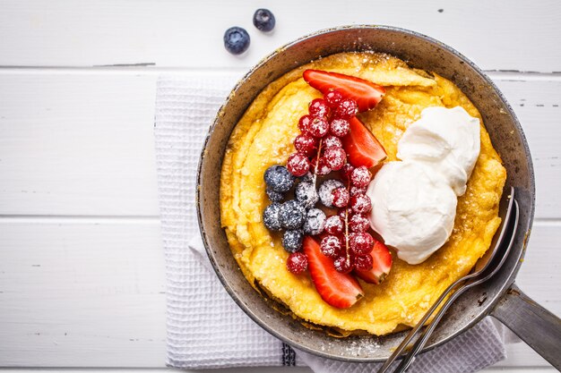 Pancake bambino olandese con bacche e panna in una padella in ghisa, vista dall&#39;alto.