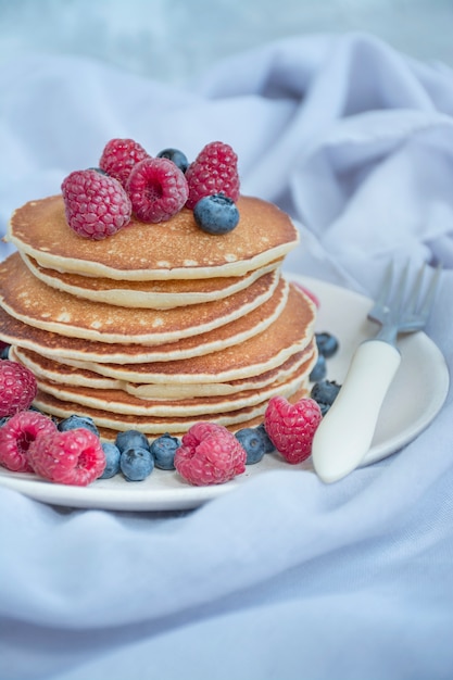 Pancake con bacche fresche su uno sfondo chiaro. Pancakes con frutta. Crepes americane tradizionali. Colazione estiva fatta in casa. Avvicinamento. L'equilibrio di un'alimentazione sana.