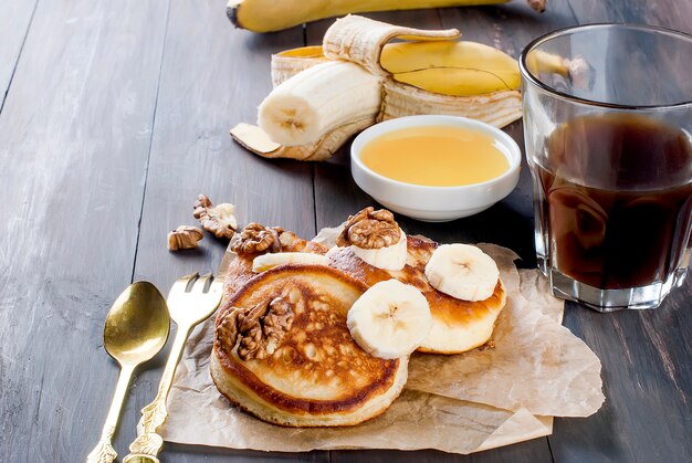 Pancake con banana, noci, miele e tazza di caffè sul buio