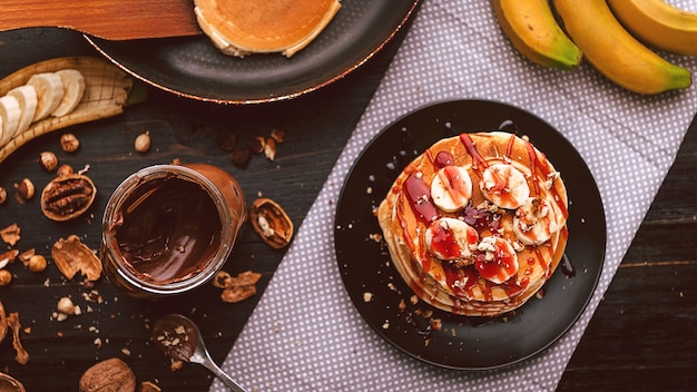 Pancake con cioccolato e pasta di noci, noci e banana su un piatto nero