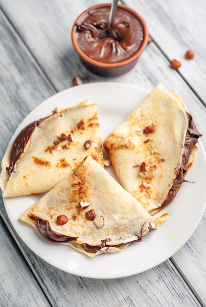 Pancake con crema spalmabile al cioccolato e nocciole, su un piatto bianco su uno sfondo di legno