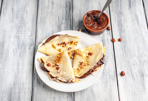 Pancake con crema spalmabile al cioccolato e nocciole, su un piatto bianco su uno sfondo di legno