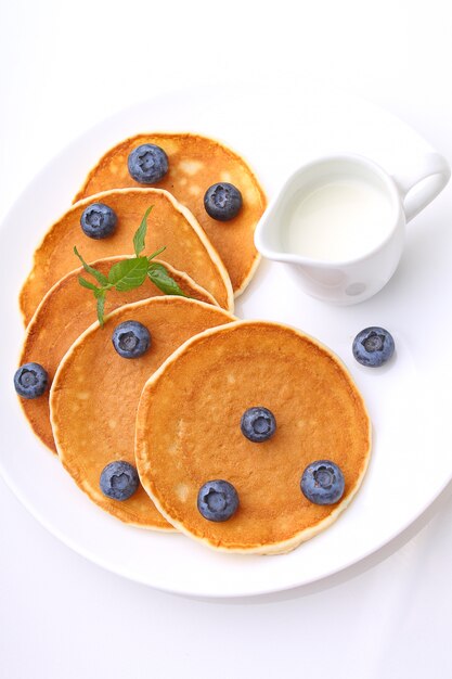 Pancake con i mirtilli delle bacche in una zolla su una priorità bassa bianca