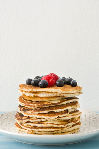 Pancake con i mirtilli ed i lamponi sulla tavola di legno blu