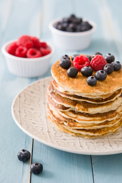 Pancake con i mirtilli ed i lamponi sulla tavola di legno blu