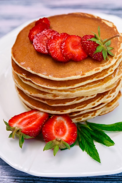 Pancake con la fragola e la menta fresche sul piatto bianco su fondo di legno blu.