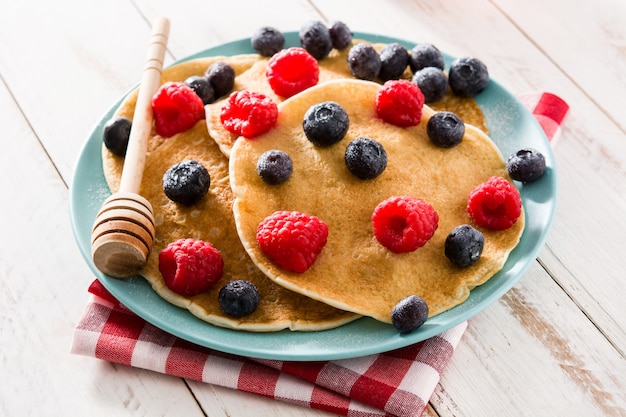 Pancake con lamponi, mirtilli e miele sulla tavola di legno bianco.