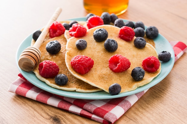 Pancake con lamponi, mirtilli e miele sulla tavola di legno.