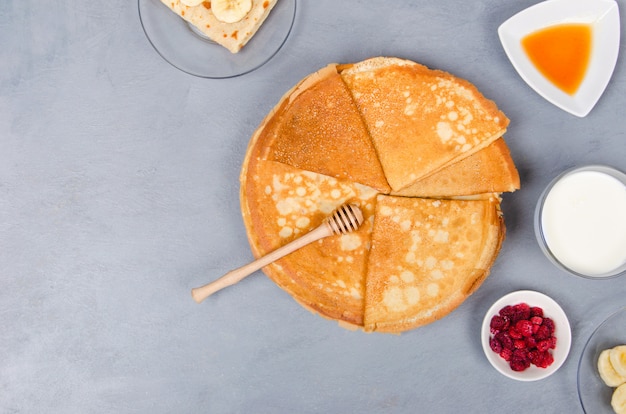 Pancake con le bacche e il miele per la prima colazione sulla tavola grigia bianca