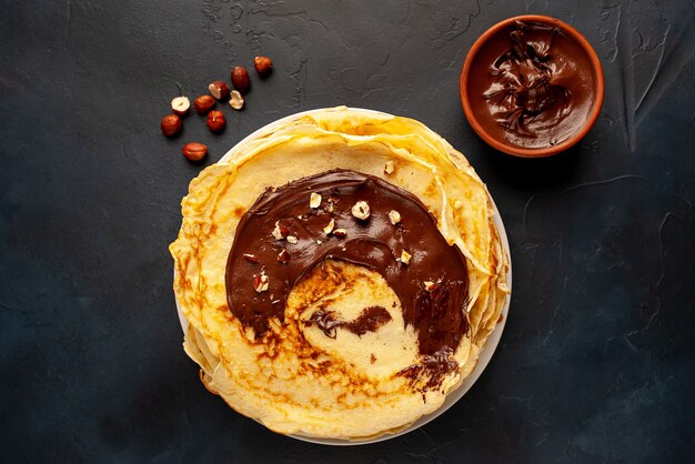 Pancake con pasta di cioccolato e nocciole, su un piatto bianco su uno sfondo di cemento, ardesia