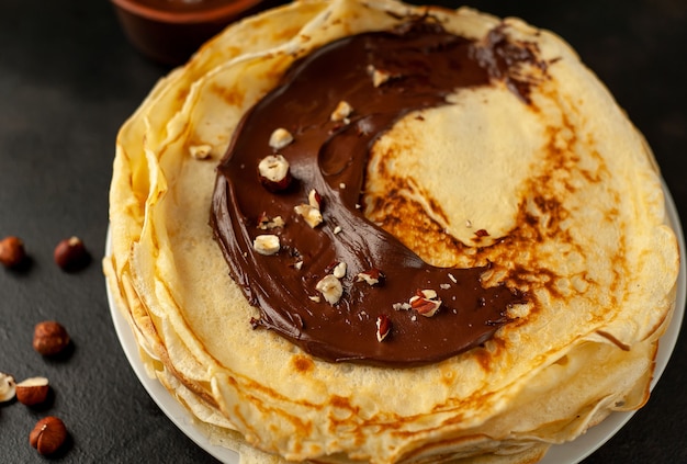 Pancake con pasta di cioccolato e nocciole, su un piatto bianco su uno sfondo di cemento