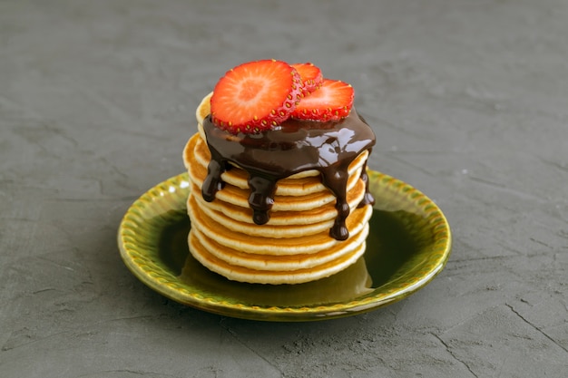 Pancake con salsa di cioccolato e fragole su uno sfondo grigio.