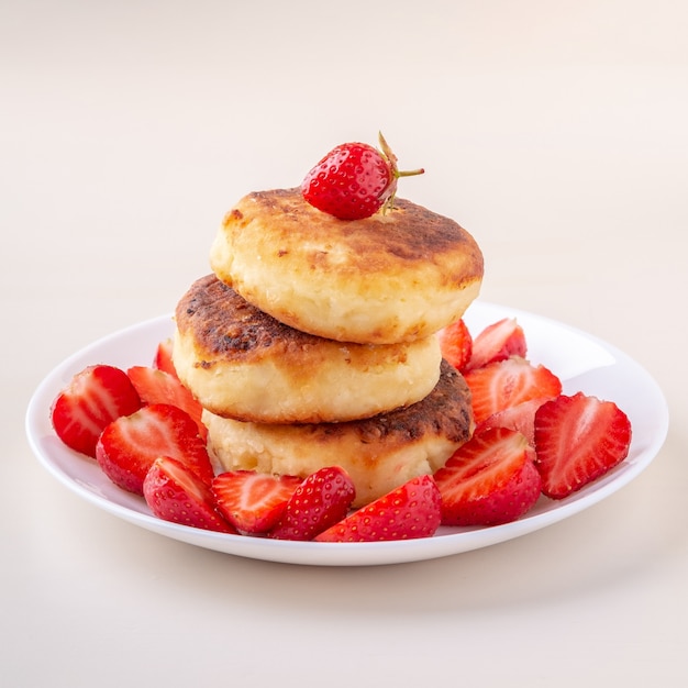 Pancake della ricotta con le fragole affettate sulla vista di angolo isolata piatto bianco