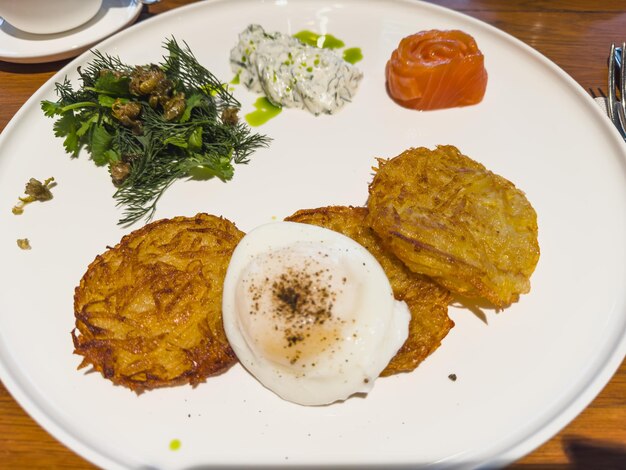 pancake di patate con salmone uova fritte erbe e salsa piccante su un piatto bianco colazione sana