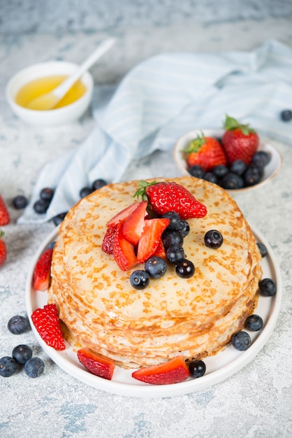 Pancake fatti in casa sottili in un piatto con bacche fresche e miele.