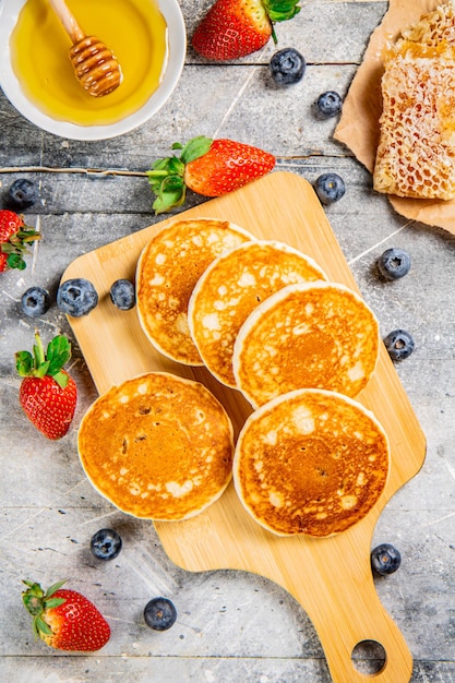 Pancake fatti in casa su un tavolo da taglio con miele e bacche