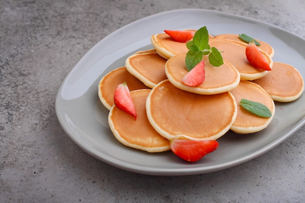 Pancake in un piatto con fragole decorate con menta su un tavolo di cemento