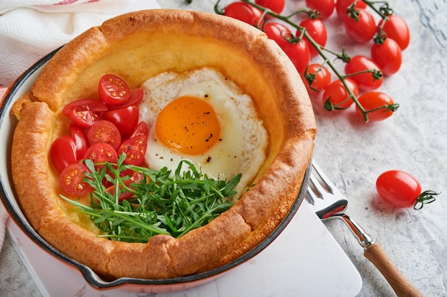 Pancake per bambini olandesi Pancake per bambini olandesi freschi fatti in casa con pomodoro uovo fritto e rucola verde in padella di ghisa a lamella su tavolo rustico in cemento grigio chiaro Disposizione piatta da vicino