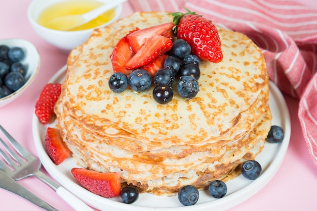 Pancake russi tradizionali sottili su una superficie rosa alla moda con bacche e miele. Avvicinamento