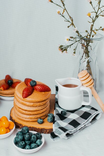 Pancake sani con fragole mirtilli miele e carruba su sfondo bianco