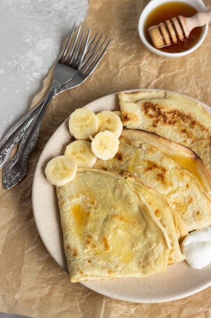 Pancake sottili con yogurt naturale, miele e banana su un piatto