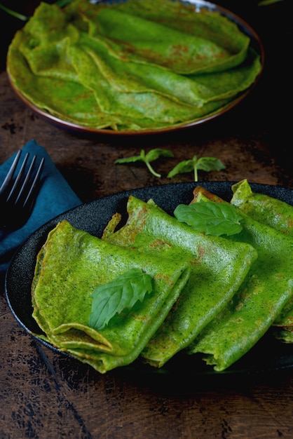 Pancake sottili di spinaci sono verdi su un tavolo di legno. Foto verticale.