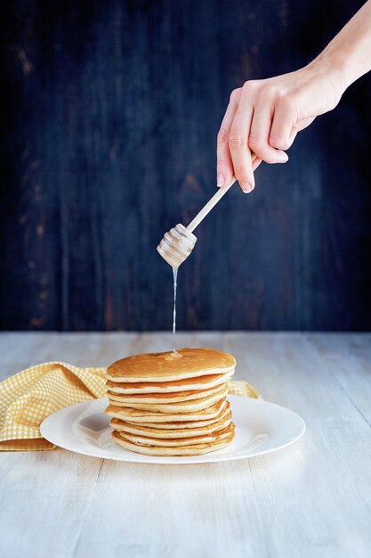 Pancake su un piatto bianco con miele su fondo di legno