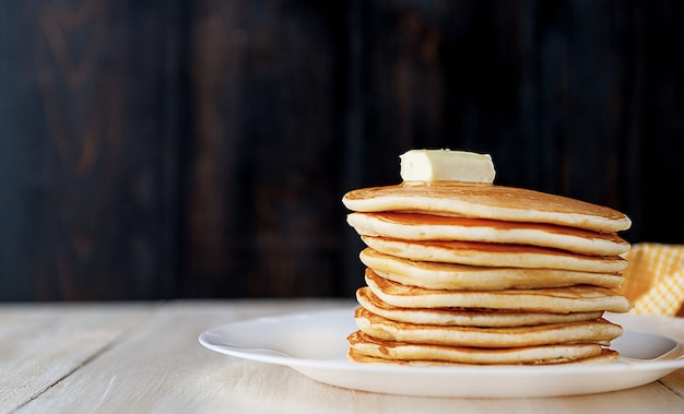 Pancake su un piatto bianco con un pezzo di burro su un fondo di legno