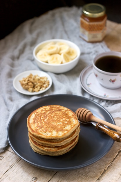 Pancakes con banana, noci e miele, serviti con tè. Stile rustico.