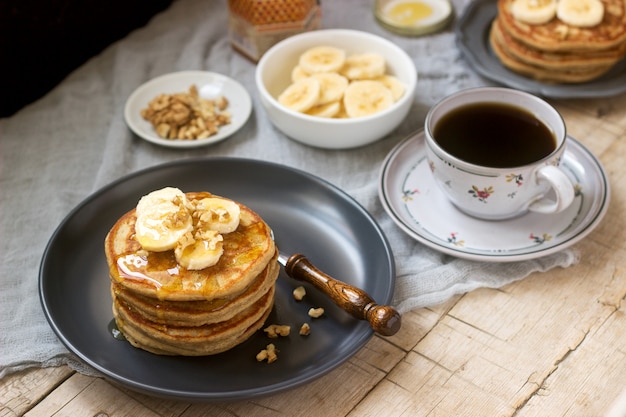 Pancakes con banana, noci e miele, serviti con tè. Stile rustico.