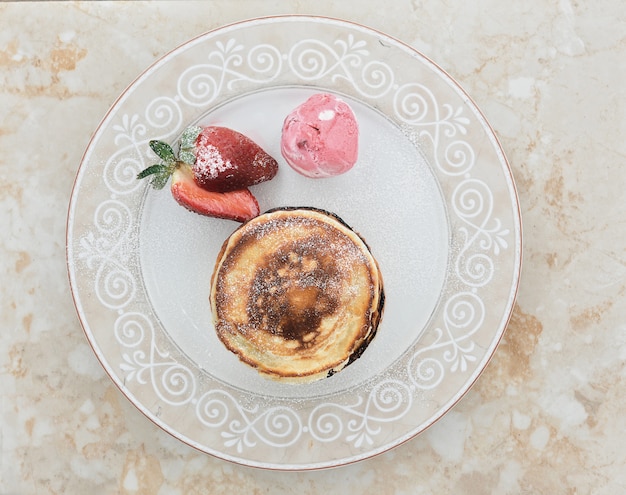 Pancakes con fragole, cosparsi di vaniglia e una pallina di gelato sul piatto