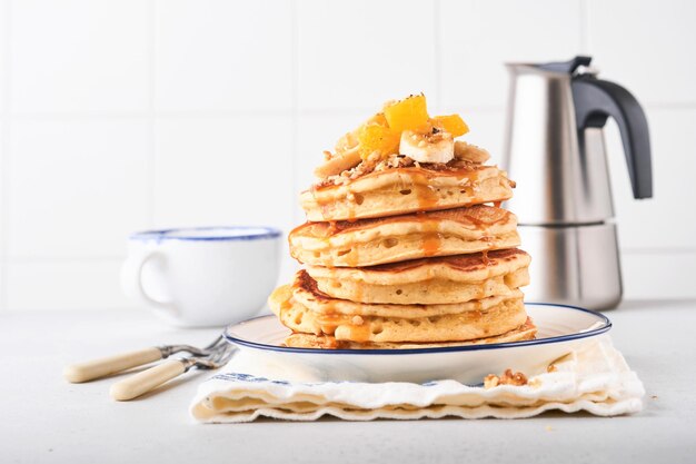 Pancakes. Pancake soffice fatto in casa con banana, noci e caramello per colazione su fondo di cemento chiaro. Deliziose frittelle per la tradizionale colazione americana. Messa a fuoco selettiva. Modello.