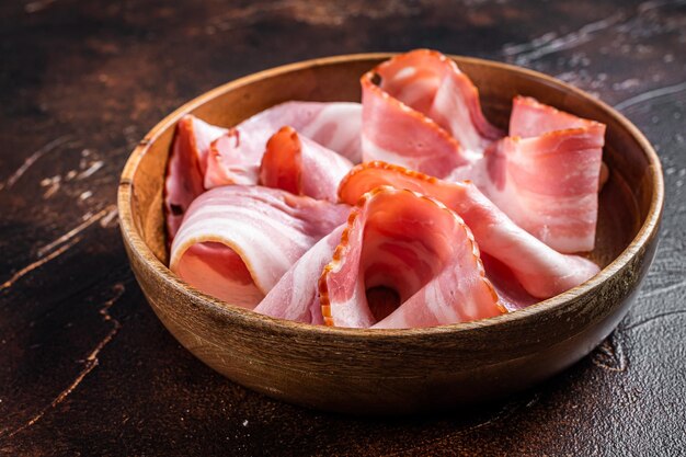 Pancetta affettata affumicata in piatto di legno. Sfondo scuro. Vista dall'alto.