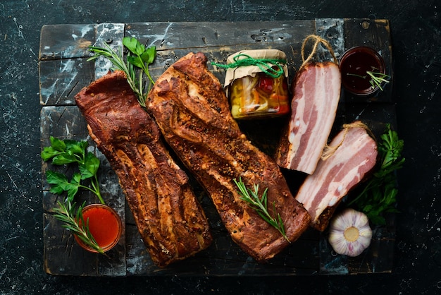 Pancetta affumicata con spezie. Pezzo di carne affumicata su uno sfondo di pietra nera. Vista dall'alto.