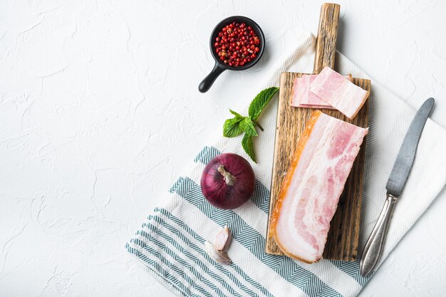 Pancetta affumicata, lastra intera con erbe su sfondo bianco, vista dall'alto con spazio per il testo.