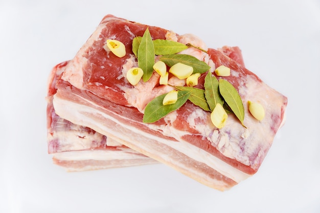 Pancetta di maiale cruda disossata con aglio e foglie di alloro isolati su sfondo bianco.