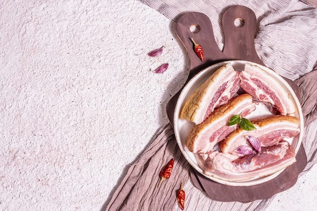 Pancetta di suino cruda con cotenna, carne di peritoneo. Spezie ed erbe aromatiche, ingredienti per cucinare pasti sani, proteine animali. Sfondo in gesso chiaro, vista dall'alto