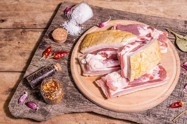 Pancetta di suino cruda con cotenna, carne di peritoneo. Spezie ed erbe aromatiche, ingredienti per cucinare pasti sani, proteine animali. Tavolo vintage in legno, vista dall'alto