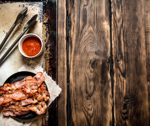 Pancetta fritta in padella e salsa di pomodoro. Su un tavolo di legno.